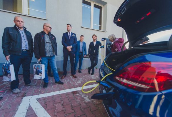 Grupa ludzi stojących obok siebie przy punkcie ładowania pojazdów elektrycznych