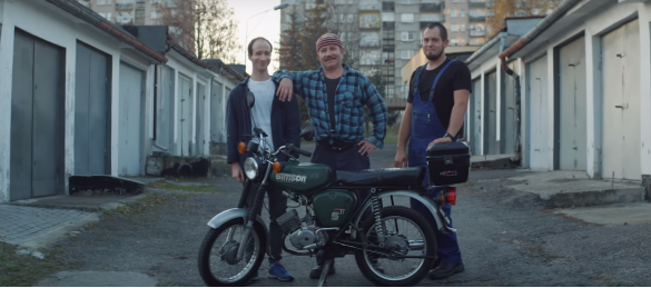 Trzech mężczyzn stojących obok siebie, przed nimi motor, w tle bloki mieszkalne