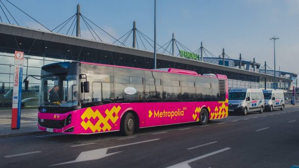 Autobus w kolorze fuksji z żółtymi elementami w tle budynek lotniska