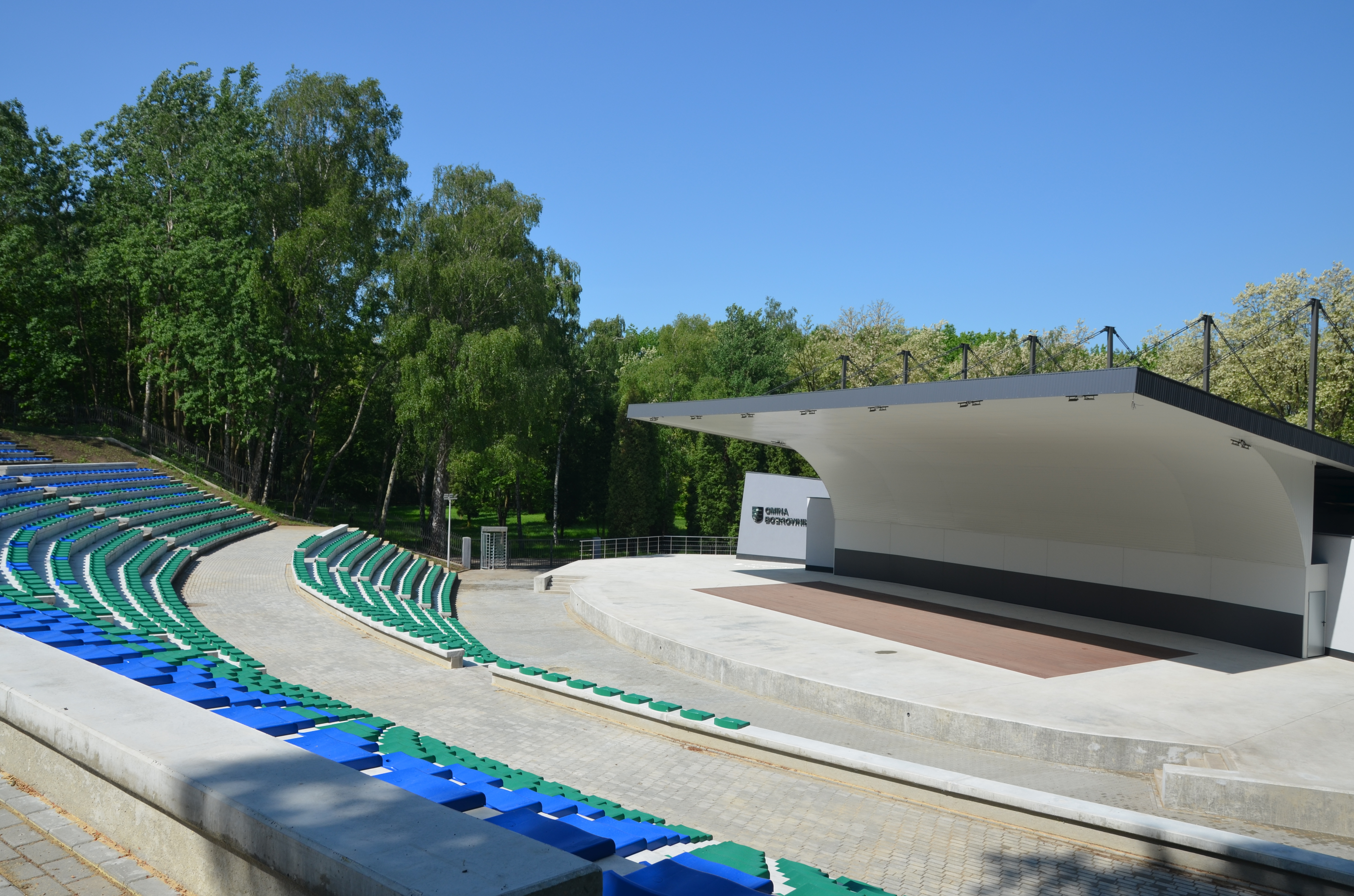 Amfiteatr z trybunami w kolorach zielonym i niebieskim oraz z zadaszoną sceną