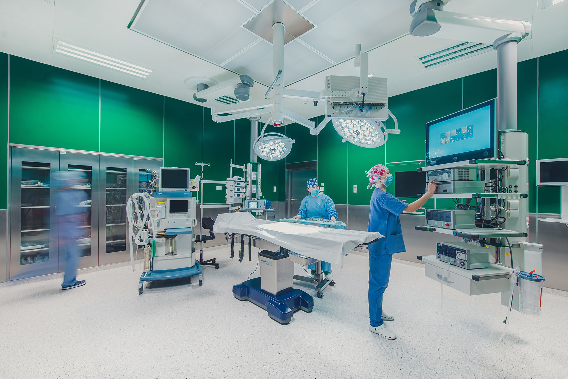 Sala operacyjna ze stołem operacyjnym po środku wokół którego stoją lekarze, w tle znajdują się urządzenia medyczne