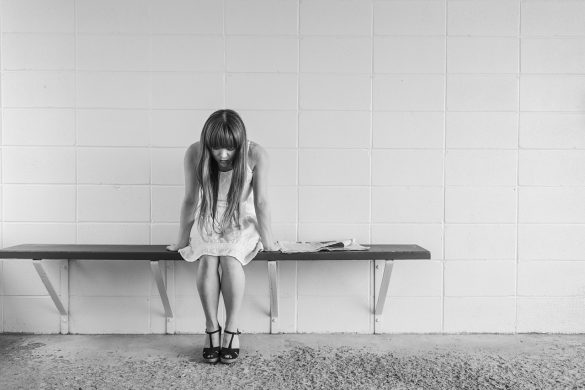 Samotna dziewczyna ze spuszczoną głową, siedząca na ławeczce