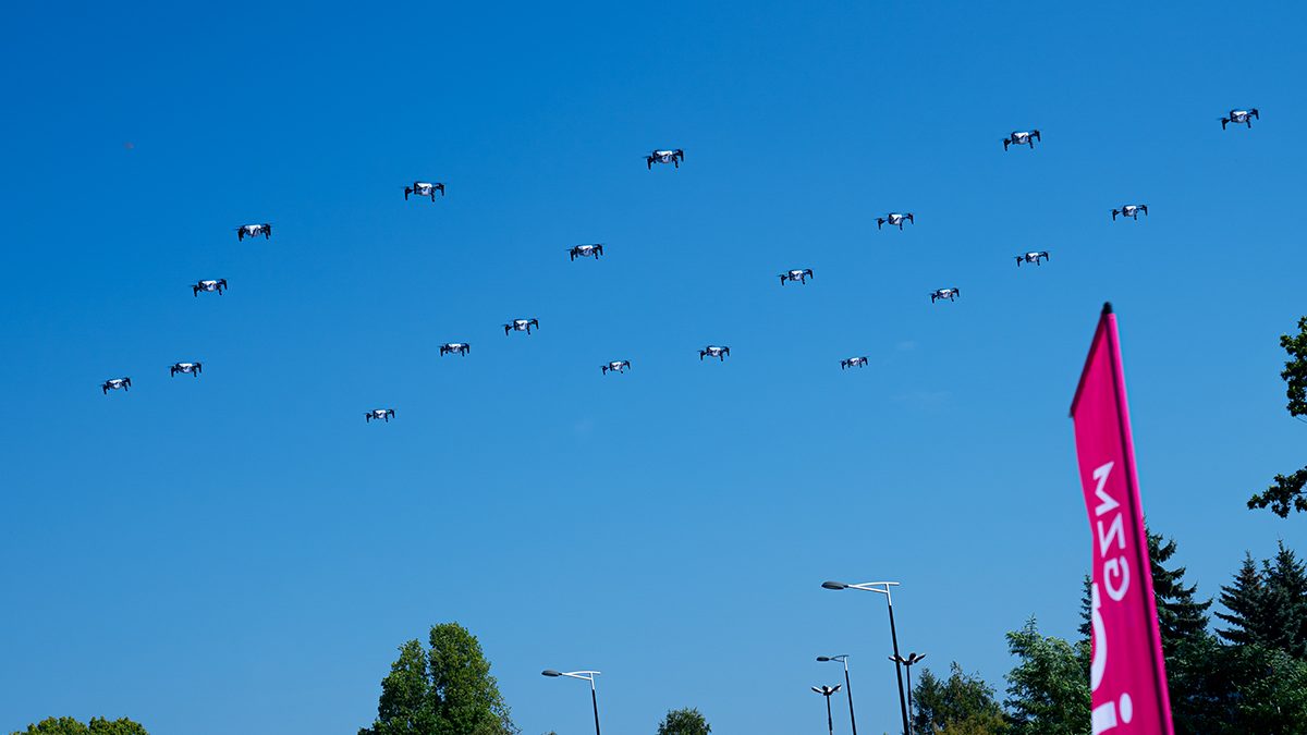Pokaz ok. 20 dronów unoszących się jednocześnie w powietrzu na tle błękitnego niebo