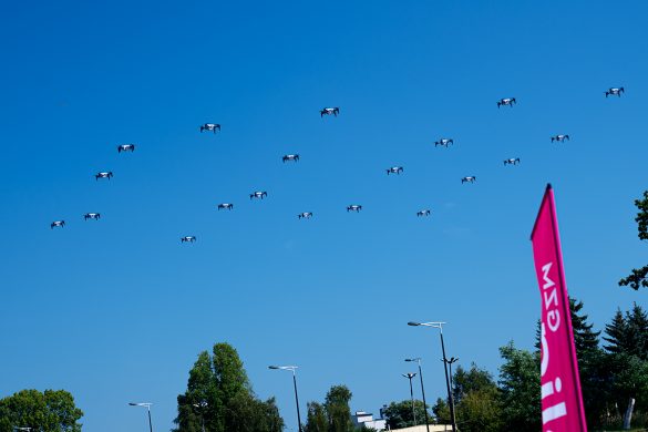 Pokaz ok. 20 dronów unoszących się jednocześnie w powietrzu na tle błękitnego niebo