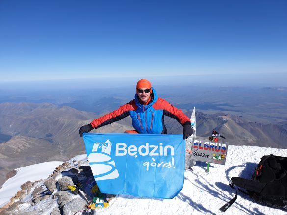 Łukasz Madej na szczycie trzymający flagę Będzin górą