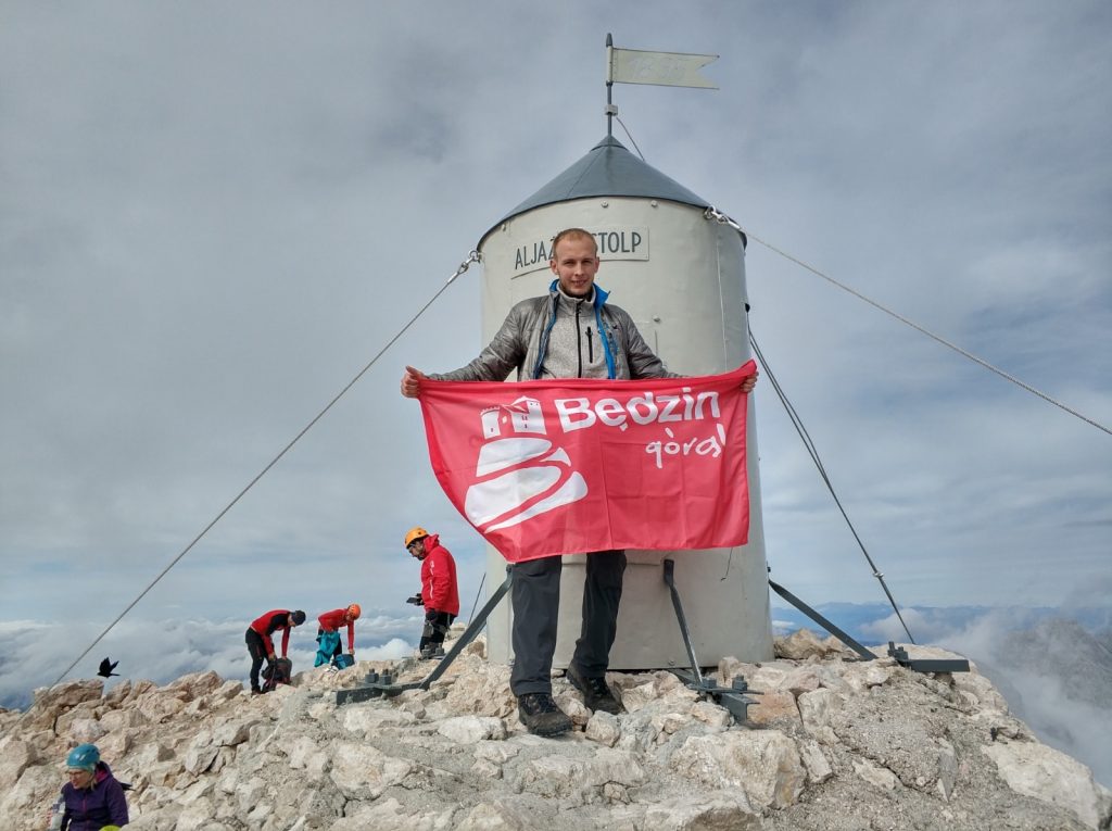 Michał Olweszak na szczycie góry z czerwoną flagą "Będzin Górą"