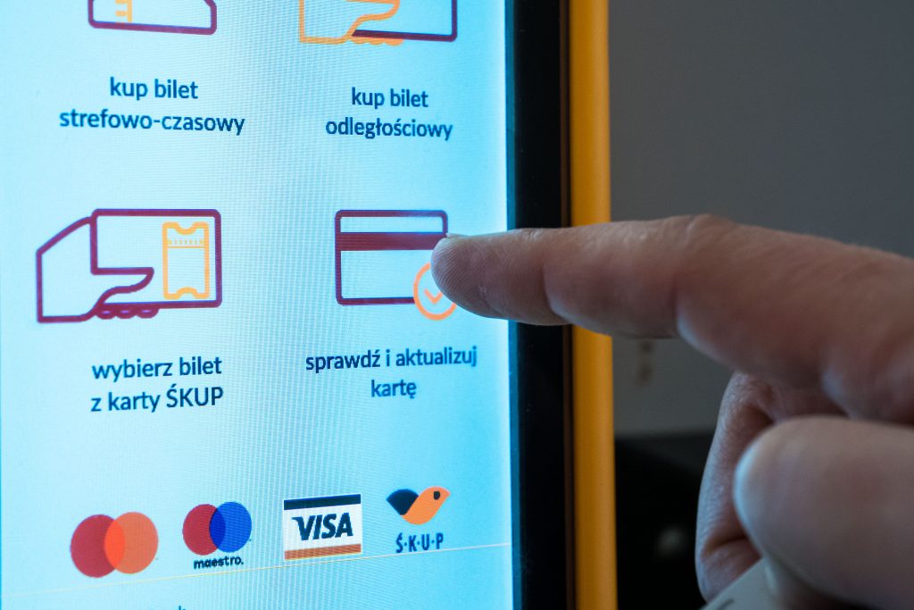 Na zdjęciu widoczny jest palec osoby, która wybiera opcję "sprawdż i aktualizuj kartę" na dotykowym ekranie nowego kasownika ŚKUP