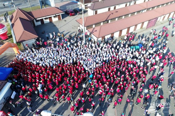 Zdjęcie z góry, uczestnicy biegu w koszulkach białych i czerwonych tworzą flagę stojąc przed startem na targowisku miejskim