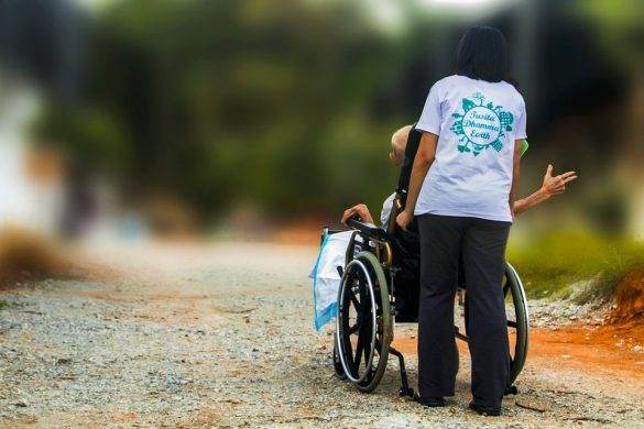 Człowiek prowadzący wózek inwalidzki z osobą niepełnosprawną