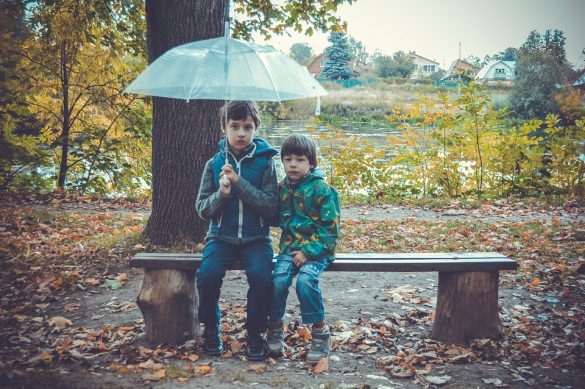 Dwóch chłopców siedzących z parasolem na ławce
