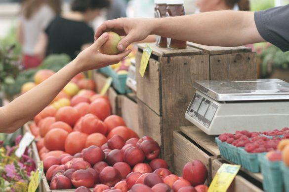 Sprzedawca podający osobie kupującej jabłko na targu