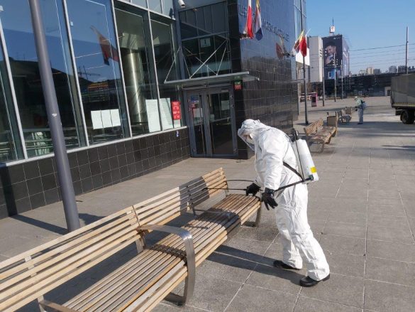 Osoba w kombinezonie dezynfekująca ławkę
