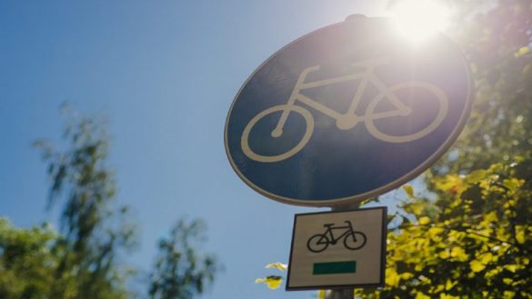 Znak informujący o drodze rowerowej zrobiony na tle drzew oraz świecącego słońca