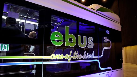 Zdjęcia przedstawia bok elektrycznego autobusu, na którego szybie znajduje się napis "EBus - one of the kind" oraz grafika wtyczki do kontaktu. Przez szybę widać ludzi stojących w środku pojazdu