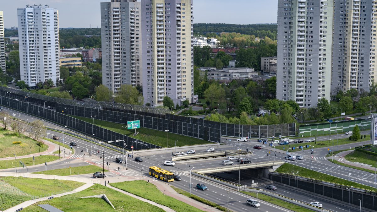 Drogowa trasa średnicowa w Katowicach, za nią osiedle Gwizdy, ulicą oprócz samochodów jedzie żółty autobus ZTM