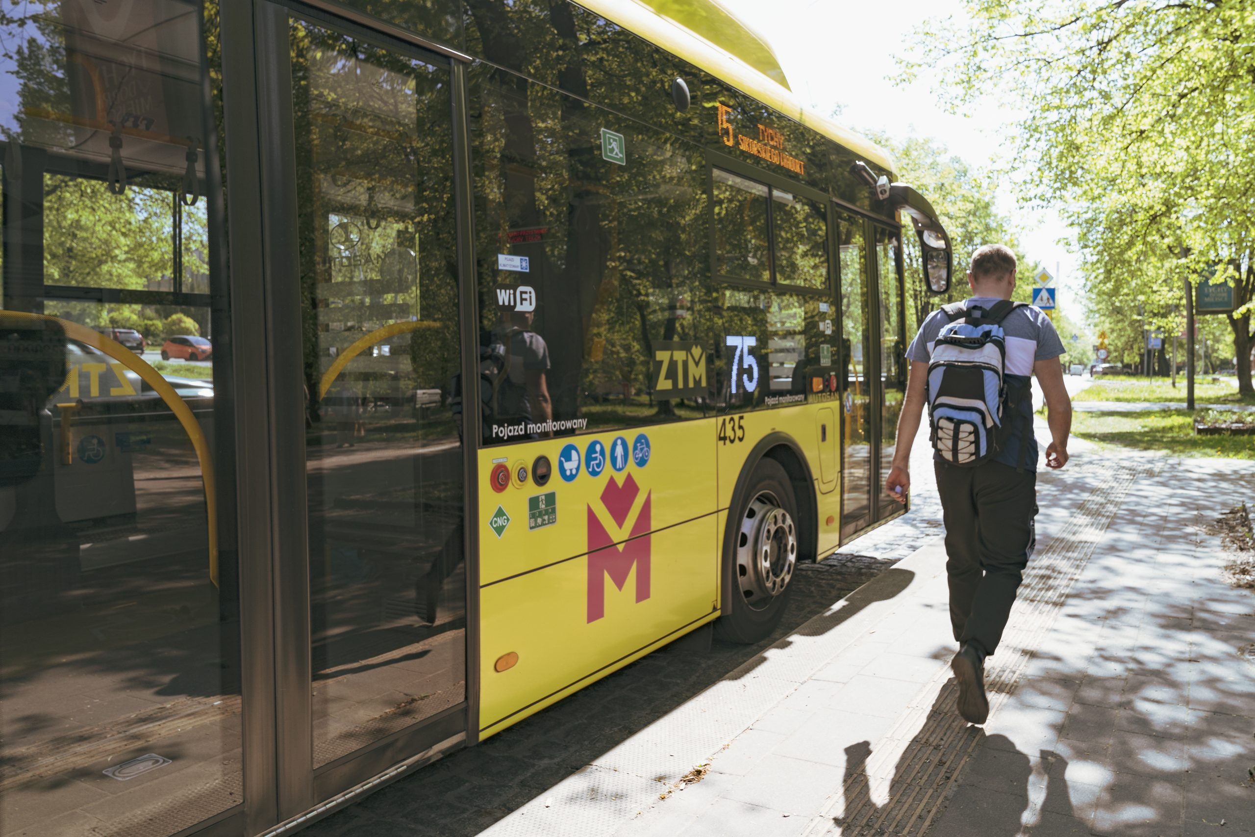Na przystanku stoi żółty autobus w logo Metropolii, obok niego mężczyzna z plecakiem