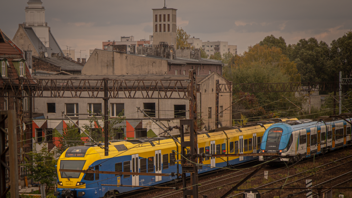 Dwa pociągi Kolei Śląskich stoją obok siebie na torach w centrum Katowic