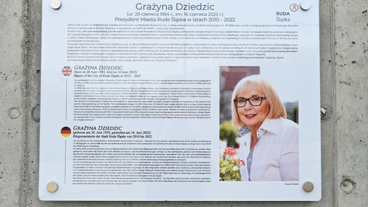 Tablica z tekstem w języku polskim, niemieckim i angielskim oraz zdjęcie połowy sylwetki kobiety w białej koszuli.
