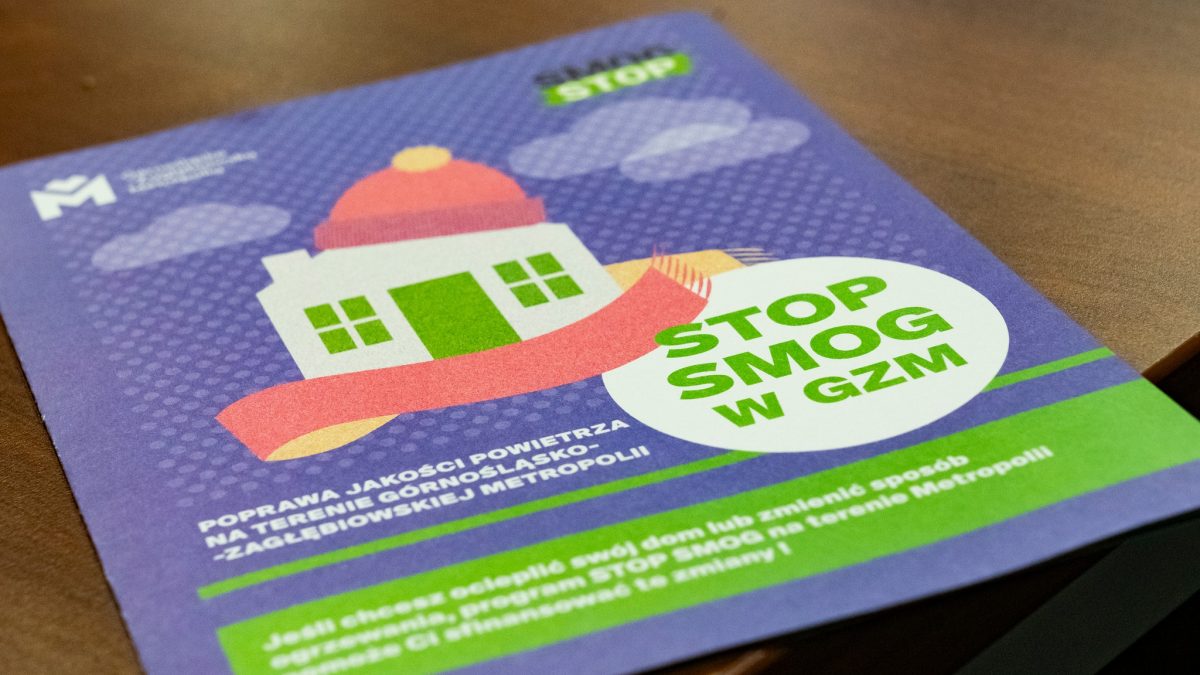 Obraz przedstawia fioletową ulotkę kampanii "STOP SMOG w GZM". Centralnie umieszczony jest rysunek domu z szalikiem, otoczonego chmurami. Tekst na ulotce informuje o poprawie jakości powietrza w Zagłębiowskiej Metropolii i programie finansowania ocieplenia domów.