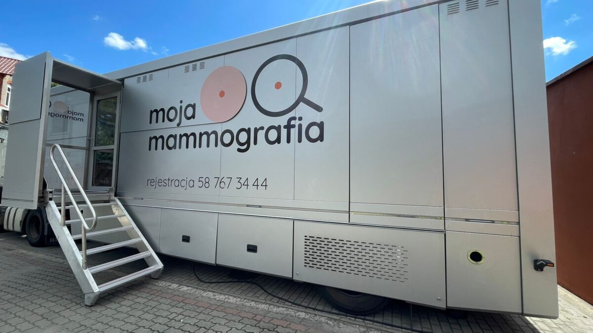 Mobilny punkt badań piersi. Srebrny mammobus z napisem „moja mammografia” i numerem rejestracji, zaparkowany na zewnątrz w słoneczny dzień.
