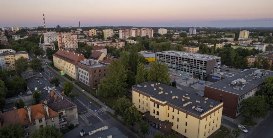 Zdjęcie przedstawia panoramę kampusu Politechniki Śląskiej w Zabrzu o zmierzchu. Widoczne są nowoczesne budynki uczelni, zieleń oraz miejska zabudowa.