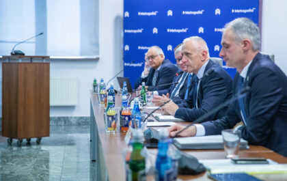 Zdjęcie przedstawia pięciu mężczyzn w garniturach siedzących przy długim stole prezydialnym na tle niebieskiej ścianki z białym logo „Metropolia”.